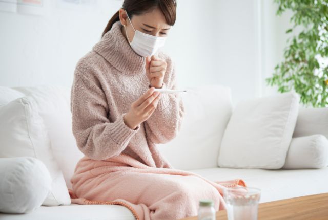 咳き込みながら体温計を見ている女性