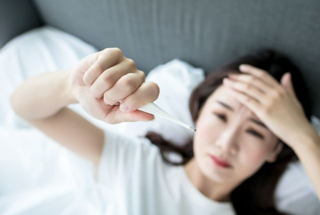 額に手を当てながら体温計を見ている女性
